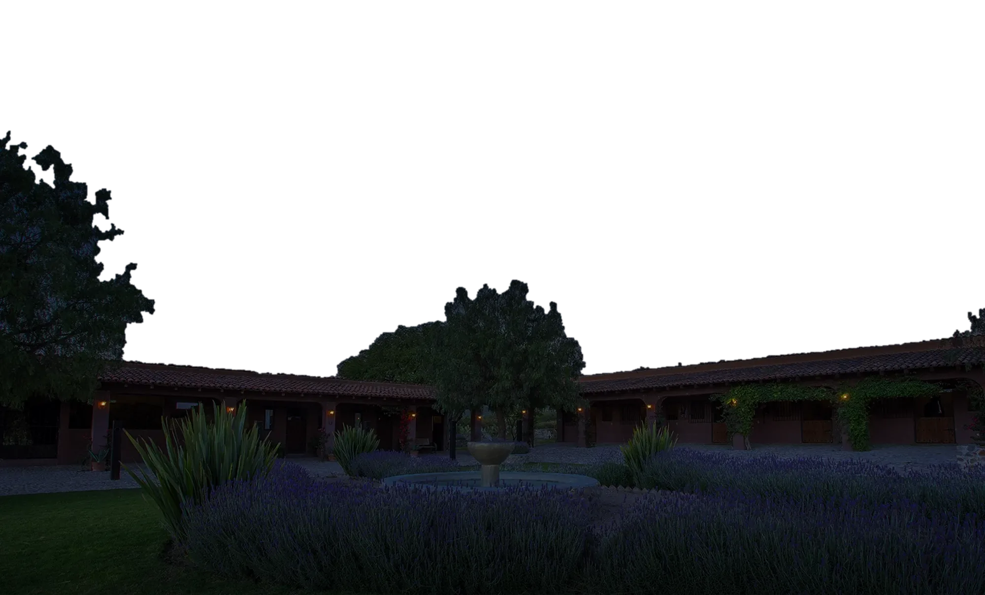 The ranch's stable courtyard at night: lavender beds around a stone fountain, lamps glowing along the portales.